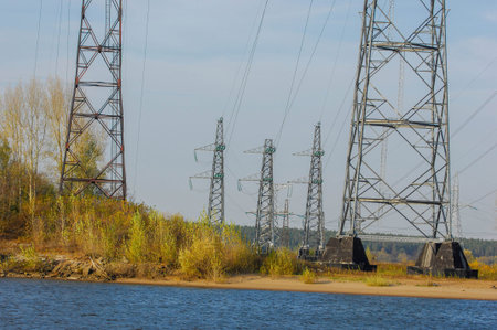 Autumn landscape, river, energy pillars, High voltage pole on blue sky background