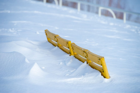 Capture the beauty of winter in a photo A sunny day illuminates a bright yellow park bench A river covered in ice and snow creates a serene atmosphereの写真素材