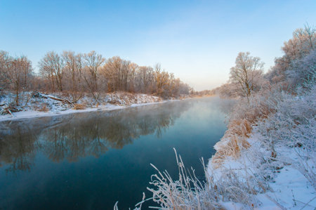Enjoy the stunning beauty of nature in all its glory. Witness the vibrant colors of the sunset reflected in the icy river. Capture unforgettable moments of winter magic and natural perfection.の写真素材