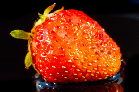 A bright and vibrant image of a strawberry on a black background. High vitamin C content and juicy taste. Ideal for promoting healthy eating or a summer fruit theme.の写真素材