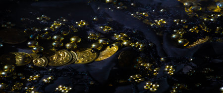Blur: An arrangement of golden coins and beads on a dark fabric background creates a striking interplay of light and shadow, adding depth and allure to this luxurious close-up.の写真素材