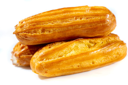 Blurred photo featuring a close-up of freshly baked eclairs resting on a white plate. The golden...