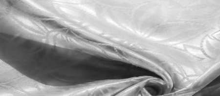 Close-up view of white satin fabric featuring a subtle leaf motif. The soft, smooth texture is...