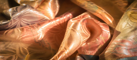 A luxurious, shiny fabric in a mix of peach, green, and gold hues with a repeating floral pattern....