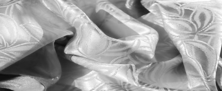 A close-up view of a shiny white fabric adorned with floral motifs, showing delicate details and...