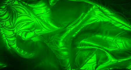A close-up of green fabric with an intricate botanical pattern, showing soft folds and light reflection for a dynamic, textured look.の写真素材