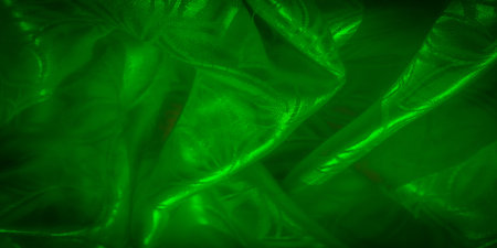 A vivid green silk fabric with a delicate leaf pattern, showing light and shadow effects across its smooth surface.の写真素材