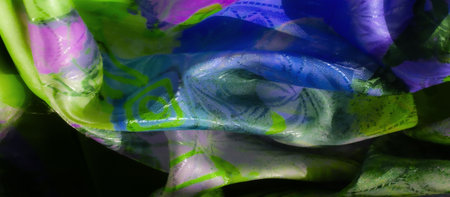 A vibrant mix of green, purple, and blue in abstract fabric patterns. The gentle folds and light reflections give depth and movement to the design.の写真素材
