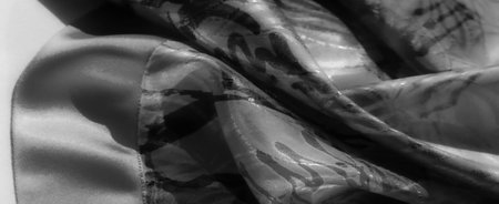 Close-up of flowing fabric with abstract black brush strokes over a patterned backdrop. Light...