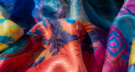 Bright, vibrant abstract fabric with bold splashes of color in shades of yellow, red, blue, and purple. Soft sheen and intricate textile folds create a dynamic artistic appearance.の写真素材