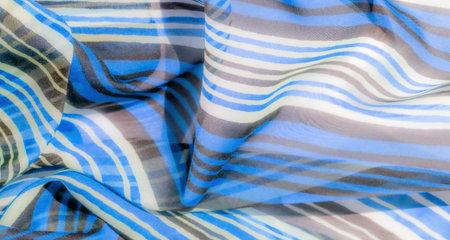 A close-up of translucent fabric with horizontal blue, brown, and white stripes, capturing its...