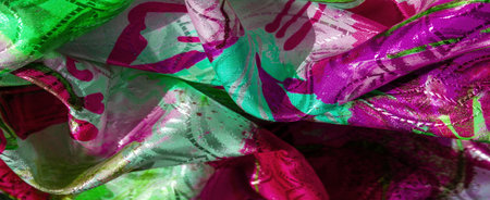 Richly colored green and magenta fabric with dynamic folds and shimmering texture. The intricate patterns are accentuated by the light, creating a sense of depth and movement.の写真素材