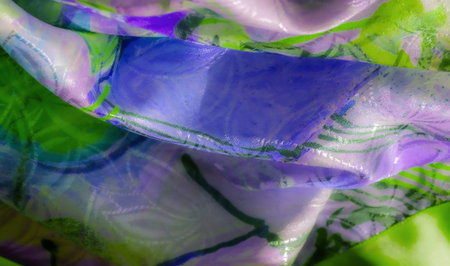 A colorful display of purple and green fabric in soft folds, with bright highlights reflecting the...