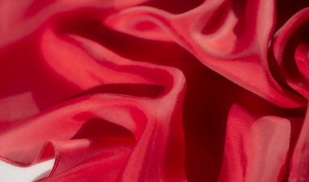 A detailed shot of red fabric with smooth, flowing folds. The vibrant red color and silky texture create a dynamic and luxurious feel, perfect for fashion or textile design concepts.の写真素材