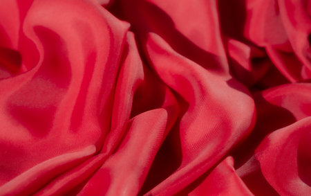 A close-up of vibrant red fabric featuring intricate folds and textures. The smooth, silky surface reflects light softly, creating a luxurious feel that enhances its rich color and elegance.の写真素材