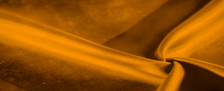 A smooth piece of golden fabric with soft folds, forming an abstract shape with deep shadows. The interplay between light and dark creates a rich and elegant visual appeal.の写真素材