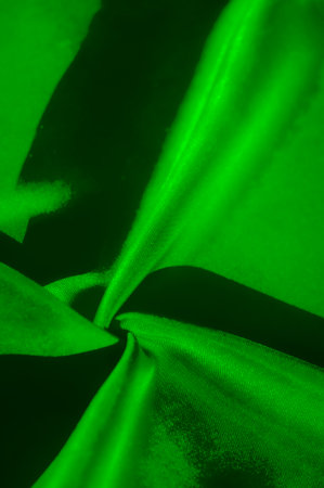 This abstract image features rich folds of fabric in a vibrant green hue, showing smooth textures and subtle shading, creating a sense of motion and depth.の写真素材