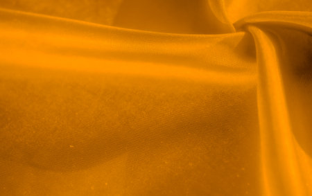A smooth piece of golden fabric with soft folds, forming an abstract shape with deep shadows. The interplay between light and dark creates a rich and elegant visual appeal.の写真素材
