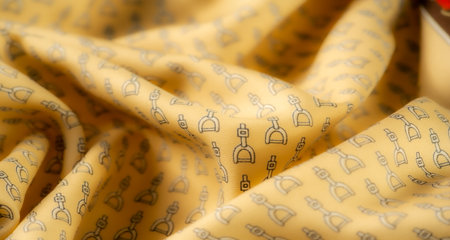 Detailed yellow fabric featuring small black stirrup designs arranged in a regular pattern. The soft ripples and shadows bring out the intricate pattern and emphasize the material's textureの写真素材