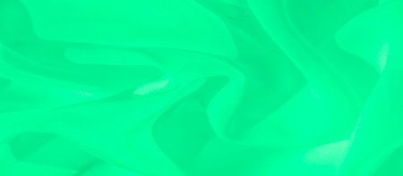 Blurred closeup of smooth green fabric gently flowing, with soft shadows creating a dynamic sense of movement. The texture is both minimal and elegant, perfect for abstract design uses.の写真素材