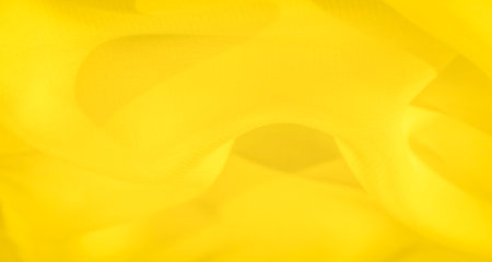 Blurred yellow fabric with a soft, flowing texture and subtle curves. The vibrant yellow color highlights the fabric's light reflection, giving it a warm, abstract composition.の写真素材