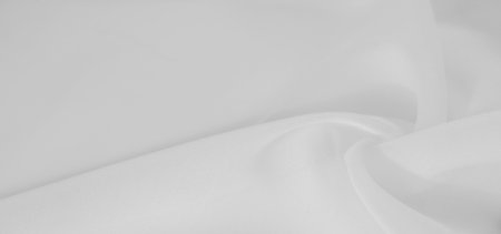 Blurred close-up of white fabric gently curving and folding, creating an organic flow with smooth textures. The soft lighting highlights the fabric's elegance and purity.の写真素材