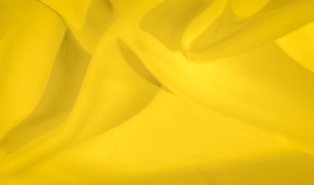 Blurred smooth yellow fabric cascades in soft folds, radiating a warm and serene ambiance. The fabric's fluidity and glowing texture make it ideal for creating peaceful backgrounds.の写真素材