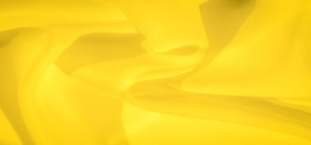 Blurred folds of yellow fabric creating gentle curves and layers, producing a soft flowing effect. The vibrant yellow color enhances the fabric's texture, evoking warmth and softness.の写真素材