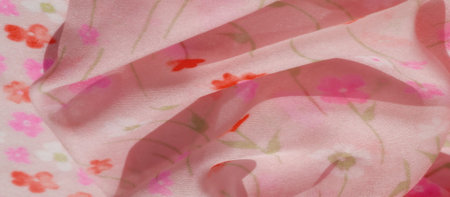 A blur of pink fabric with a floral print featuring red and pink flowers. The fabric is folded to...
