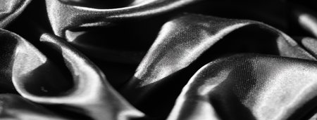 Blur of silky black fabric with light reflecting off its smooth, flowing folds. The luxurious texture and dark sheen create a refined, elegant backdrop suitable for various design projects.の写真素材