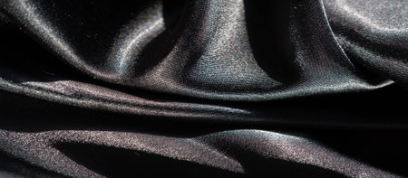 Blur of black fabric with dynamic folds creating an abstract interplay of textures and shadows. The soft reflective surface accentuates the fluid movement of the fabric's folds.の写真素材