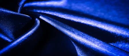 A blurry close-up of shiny blue fabric with intricate folds and smooth textures. The image captures the play of light and shadow on the shimmering fabric, enhancing its fluidity.の写真素材