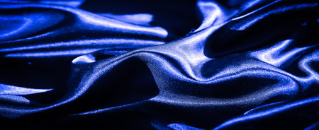Blur of silky blue fabric, flowing with soft folds and intricate texture. The sheen from the material enhances the feeling of elegance and luxury, perfect for fashion design.の写真素材