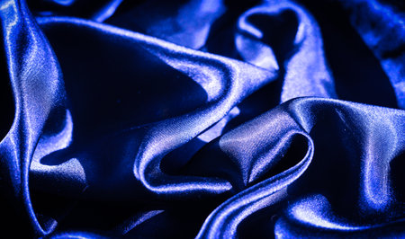 Blurred ripples of deep blue satin fabric flow in gentle waves, highlighted by bright reflections and shadows, creating a sense of luxurious softness and depth. Ideal for abstract backgroundsの写真素材