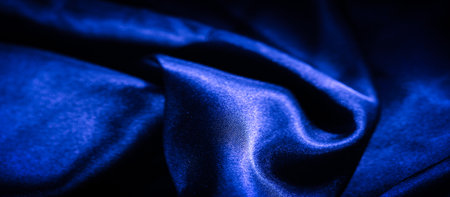 Blur of crumpled blue satin fabric forming intricate folds. The shiny texture of the fabric creates mesmerizing patterns of light, offering a soft, elegant, and luxurious visual experience.の写真素材