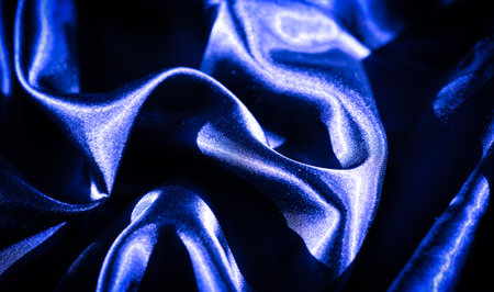 Blur of deep blue satin fabric flowing in soft waves and folds, creating a silky, glossy texture with subtle highlights, illuminated by diffused lighting for an elegant composition.の写真素材