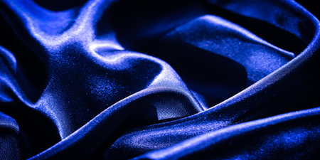 Blur of glossy, deep blue satin fabric with flowing creases. The reflective surface and rich color give the fabric a luxurious, sophisticated look, ideal for fashion or interior design.の写真素材