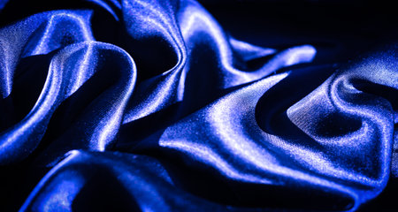 Blur of deep blue satin fabric with elegant folds and rich texture. The glossy, smooth surface reflects light, adding a touch of luxury and style to the composition.の写真素材