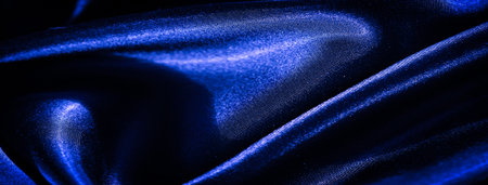 Blur a cascade of rich blue satin fabric falls in soft folds, its glossy surface reflecting light, creating an abstract play of texture and shadow, exuding opulence and grace.の写真素材