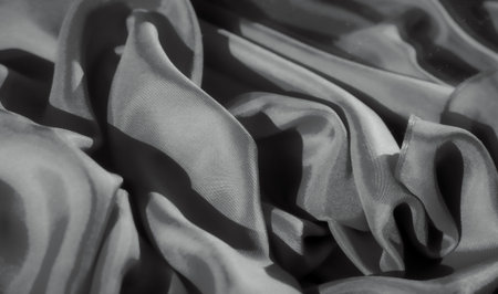 An abstract capture of soft fabric folds, with gentle curves and shadow play. The fabric's smooth surface contrasts against darker areas, creating an elegant and sophisticated texture design.の写真素材