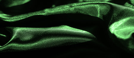 Blur of vibrant green satin fabric with soft, flowing curves. The smooth texture and shiny surface create an elegant, abstract display of light and shadow, highlighting the luxurious materialの写真素材