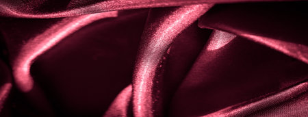 Blurred image of crimson satin fabric with smooth folds and a reflective sheen. The rich texture and deep red color of the fabric create a feeling of luxury and refinement, ideal for fashion or decor.の写真素材
