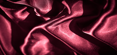 Blur of vibrant red satin fabric creating rippling folds, capturing the interplay of light and shadow. The fabric's sheen enhances the texture and luxurious appeal.の写真素材