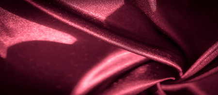 Blurred deep scarlet satin fabric with delicate folds, reflecting light to create a fluid and silky surface. Ideal for luxury design projects, textile backgrounds, and fashion visuals.の写真素材