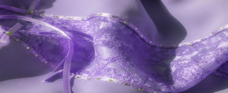 A blurry detail shot of purple lace fabric adorned with tiny shimmering beads and satin ribbon accents. The luxurious texture and elegant design create a sophisticated, romantic look.の写真素材