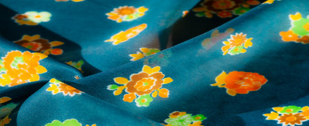 A blur of soft floral fabric with orange, yellow and green flowers on a deep turquoise background. The folds of the material highlight the texture and depth of the vibrant floral design.の写真素材