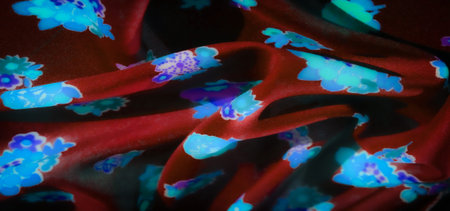 Blur of glowing blue and purple floral patterns spread across vibrant red fabric. The fabric's soft...