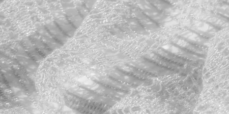 Blur of delicate lace fabric in white, showing its soft texture and intricate detailing. The...