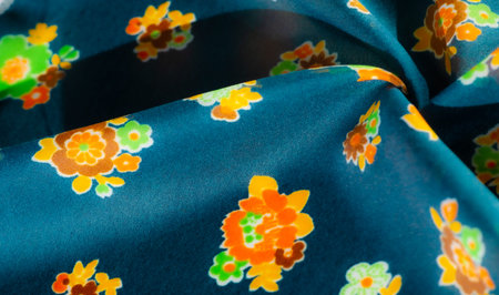 A blur of bold floral fabric with vibrant orange, green and yellow flowers on a dark turquoise...