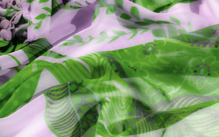Blur of translucent green and lavender fabric with abstract floral patterns, creating a soft,...